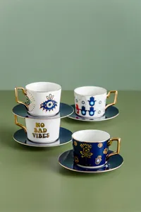 Dettaglio di tazzine da caffè in ceramica con manici dorati e motivi Evil Eye