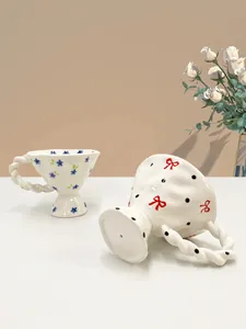 Detail of hand-painted floral and bow ceramic mugs with twisted handles and wavy edges