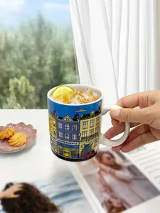 Detail of hand holding ceramic mug with colorful Italian street architecture and lemon tea