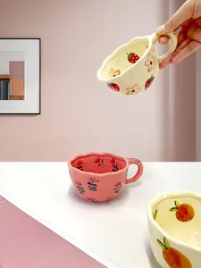 Detail of handmade ceramic strawberry coffee mug with a thick round handle and wavy rim