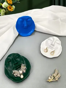 Artistic face-shaped trays displaying pearl butterfly brooches and drop earrings on silk
