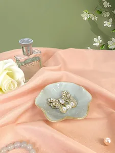 Dettaglio della spilla a farfalla dorata con perle e zirconi su un vassoio di ceramica
