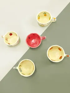 Top view of five handmade ceramic coffee mugs with various hand-painted fruit and flower motifs