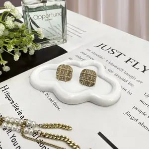 Detail of square gold earrings with pearls and rhinestones on a white cloud tray