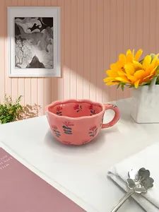 Close-up of pink ceramic strawberry cup with wavy edge and floral metal spoon