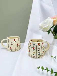 Close-up of handmade irregular ceramic mugs with hand-painted rose and tulip floral patterns