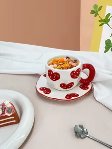 Detail of hand-pinched ceramic coffee cup with red hearts and matching floral spoon