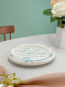 Detailed top view of a white ceramic plate with hand-drawn blue bow and ribbon patterns