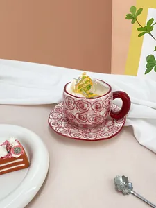 Detailed view of hand-pinched ceramic coffee cup set with red rose pattern and wavy saucer
