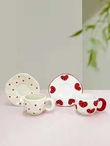 Macro view of handmade ceramic coffee cup sets with red heart patterns and wavy edges