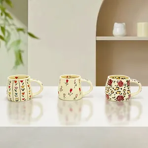 Three handmade ceramic coffee mugs with floral and leopard patterns on cream white base