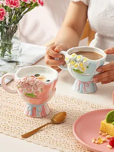 Nahaufnahme von Keramiktassen mit Blumenrelief und Schleifenfuß auf einer Spitzendecke