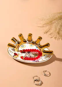 Bandeja de cerámica ojo turco con soporte de anillos dorado sobre fondo rosa