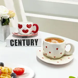 Handmade ceramic coffee cup and saucer set with red heart patterns and wavy edges