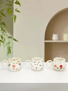 Detail of handmade ceramic mugs with wavy rim, ring handle, and floral patterns