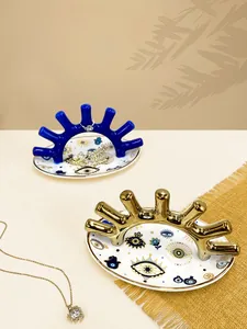 Detalle de bandejas de cerámica para joyas con motivo de ojo y soportes dorados