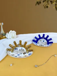 Detalle de bandeja de cerámica para joyas con soporte dorado para anillos y diseño de ojo