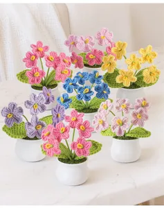 Macro detail of six colorful handmade crochet forget-me-not potted flowers on marble
