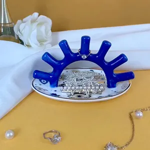 Soporte de joyas coral azul con bandeja cerámica de ojo sobre fondo de seda amarilla y blanca