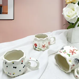 Three handmade ceramic coffee mugs with floral patterns and wavy rims in a cozy home setting