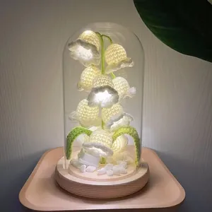 Close-up of handmade crochet Lily of the Valley night light in glass dome with wood base