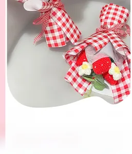 Détail macro d'un bouquet de fraises crochetées main dans un emballage cadeau à carreaux