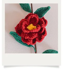 Détail macro du camélia rouge tricoté main avec cœur doré et feuilles de laine verte