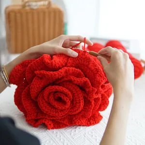 Close-up of hand-knitting a large red crochet rose with yarn and a crochet hook