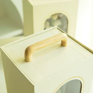 Detalle de caja de regalo crema con asa de madera y ventana transparente arqueada