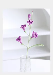 Detail of handcrafted purple crochet freesia flowers with green stems in a glass vase