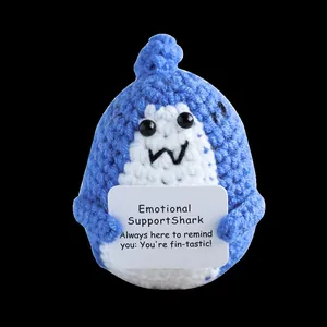 Detailed close-up of a blue crochet shark doll holding an encouraging message card