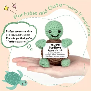 Handmade crochet turtle plush with motivational card held in palm on pink background