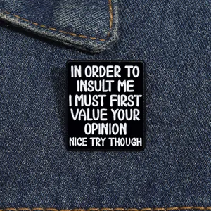 Detail of a rectangular black enamel pin with white quote on dark denim fabric
