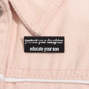 Detail der Educate Your Son Anstecknadel aus schwarzem Emaille auf rosa Jeansstoff