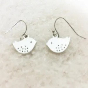 Minimalist silver bird dangle earrings with hollow dot pattern on white faux fur background