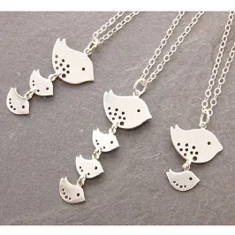 Detailed view of silver bird pendants on delicate chain necklaces with stone background