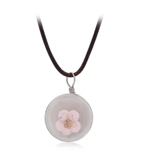Collier artisanal en résine avec véritable fleur séchée rose et cordon tressé sur fond blanc