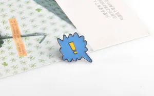 Detail of blue comic bubble enamel pin with yellow exclamation mark on floral card