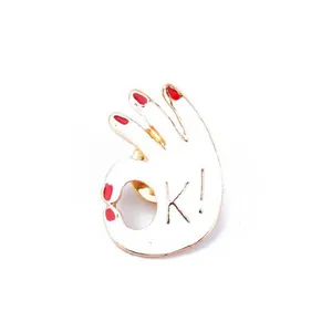 Detailed view of an enamel OK gesture pin with gold plating and red nail polish accents
