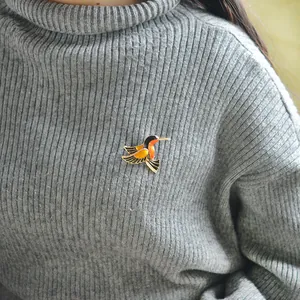 Schicke Kolibri Brosche mit schwarz-orangefarbener Emaille auf grauem Strickpullover