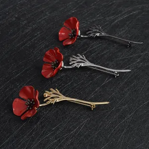 Vibrant red poppy flower brooches with gold, silver and black metal stems on dark background