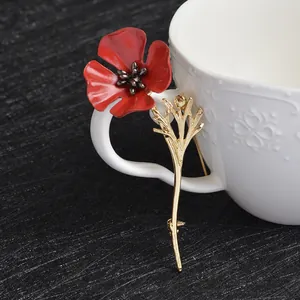 Elegant red enamel poppy flower brooch with golden stem on a white ceramic mug handle