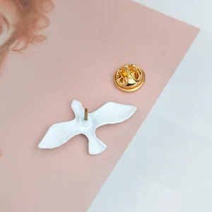 Minimalist white flying bird brooch pin with golden butterfly clutch backing