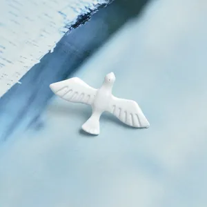 Detailed view of flying white dove enamel brooch with feather textures on light blue background