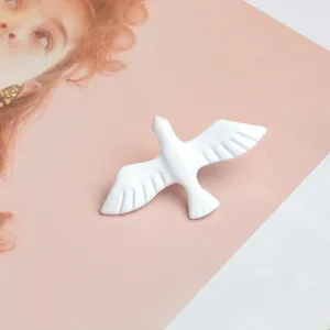 Detail of white ceramic-textured peace dove brooch with feather texture on pink background