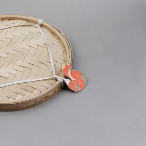 Detailed close-up of a fox-shaped enamel brooch on a woven bamboo tray with gray texture