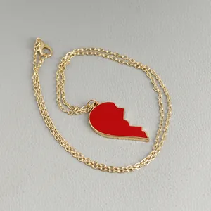 Minimalist gold necklace featuring red enamel heart pendant on a leather surface