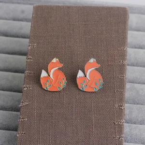 Charming orange enamel fox brooches with green leaves on a textured card holder