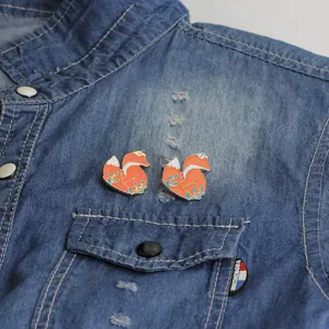 Charming enamel fox brooches with orange-red detail on a blue denim shirt