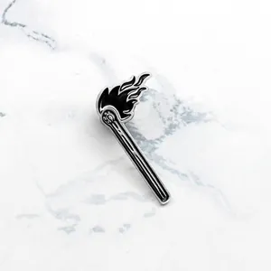 Cartoon black enamel burning matchstick brooch pin with silver alloy accents on marble